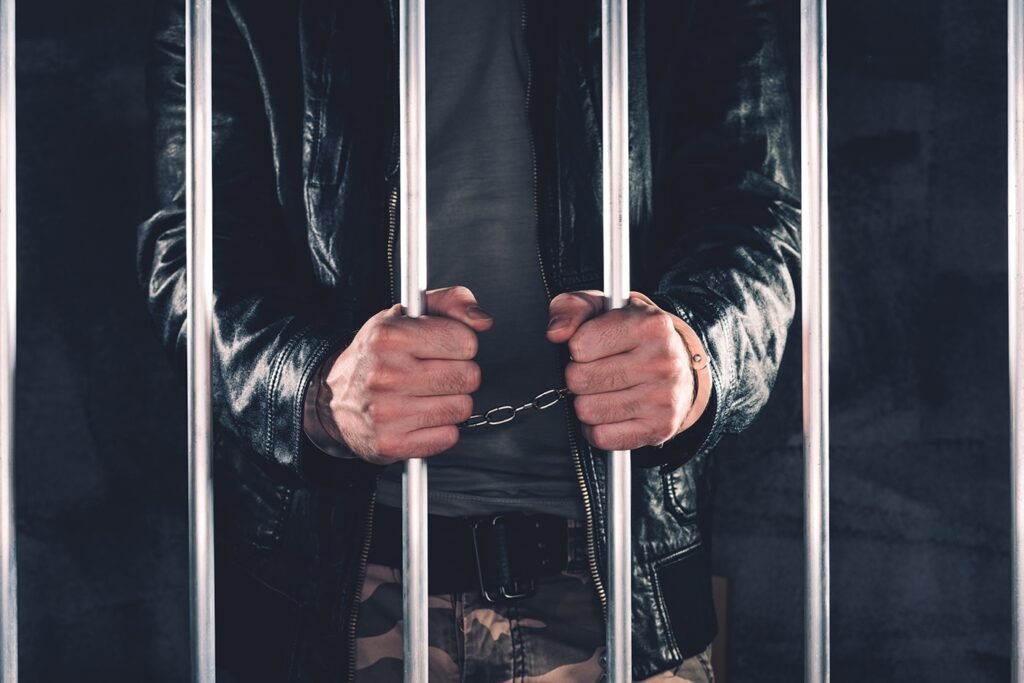 Persona detrás de barrotes con las manos esposadas